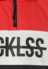 Giacca rossa, bianca e nera con una cerniera nera e audaci lettere nere che spellano "CKLSS" sulla sezione bianca attraverso il petto.