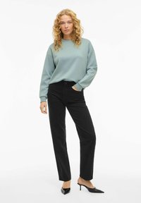 Svetlo modra majica z dolgimi rokavi, kombinirana z visokim pasom črnimi kavbojkami in črnimi koničastimi petami. Preprost dizajn in gladka tekstura.