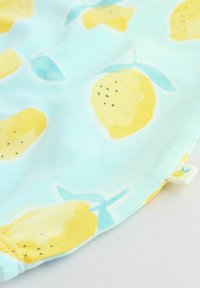 Blåt stof med mønster af gule citroner, indeholdende grønne blade og sorte prikker. Inkluderer en lille mærkat med en ananasgrafik.