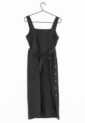 Ein schwarzes, ärmelloses Kleid mit quadratischem Ausschnitt, einem taillierten Gürtel und einer Knopfleiste an der Seite mit sechs Knöpfen. Strukturierter Stoff.