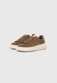 Brown suede sneakers with flat laces and a chunky cream rubber sole. Features a logo on the tongue and tonal stitching on the upper.