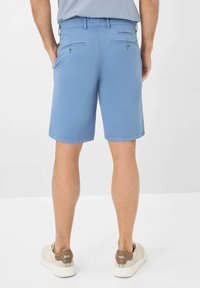 Pantaloni corti in cotone blu con davanti piatto e due tasche posteriori, dotati di bottoni. Indossati con sneakers beige, che mostrano una texture pulita e liscia.