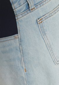 Tecido de denim azul claro com painel contrastante azul escuro e costura laranja. Apresenta um botão prateado e bolsos funcionais.