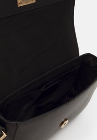 Borsa a mano nera in pelle con una chiusura in metallo dorato, dotata di un ampio scomparto interno e una tasca laterale, texture liscia.