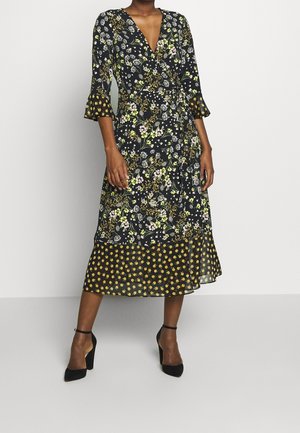 Femme portant une robe midi noire à fleurs avec des manches trois-quarts et des chaussures à talons noirs.