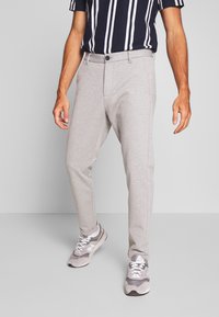Pantalones elásticos grises de corte slim con bolsillos laterales, combinados con una camisa de manga corta a rayas en tonos azul marino y blanco. Combinados con zapatillas grises.