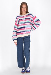 Mehrfarbiger gestrickter Pullover mit einem Rautenmuster in Pastellfarben, locker sitzend mit einem gerippten Saum, kombiniert mit weit geschnittenen blauen Jeans.
