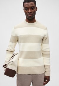 Hellbeige gestreifter Pullover mit gerippter Textur, rundem Ausschnitt und langen Ärmeln, kombiniert mit einer beige-braunen Tragetasche.
