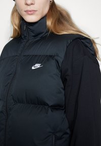 Gilet trapuntato nero con colletto alto, chiusura con zip e logo Nike sul petto. Presenta una texture trapuntata e un morbido rivestimento interno.