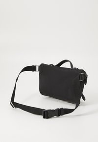 Black rectangular crossbody bag made of textured material. Features a detachable strap, leather accents, and a small handle.