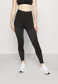 Zwarte high-waisted leggings met geribbelde textuur en mesh accenten. Ze hebben een gevormd ontwerp en zijn gecombineerd met witte sportschoenen.