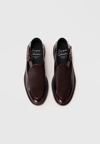 Dark brown leather shoes featuring a smooth finish, a large fur-covered toe cap, and a buckle strap with a contrasting texture.