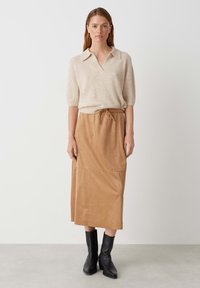 Maglione beige lavorato a maglia con colletto e maniche corte, abbinato a una gonna midi color crema con cintura elastica. Stivali neri alla caviglia.