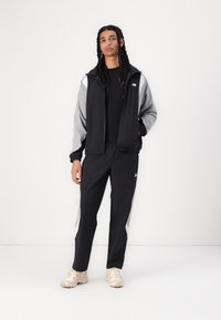 Black and gray tracksuit with a zip-up jacket and elastic waistband pants. Features a logo on the chest and side panels. Lightweight fabric.