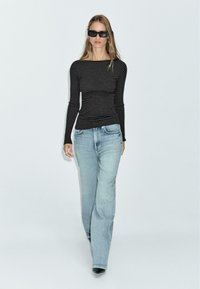 Zwart en grijs gestreepte langemouwen top met een off-shoulder ontwerp, gecombineerd met lichtblauwe losse spijkerbroeken en zwarte puntige hakken.