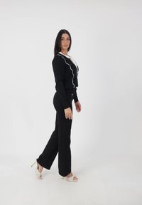 Conjunto negro que incluye una blusa ajustada con ribetes blancos y un lazo, combinada con pantalones anchos negros y sandalias de tacón alto beige.