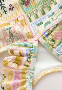 Mehrfarbiger, gesteppter Stoff mit Blumen- und geometrischen Mustern; verfügt über einen gerafften Akzent; weiche Textur, pastellfarbene Schattierungen in Pink, Grün und Gelb.