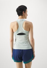 Lichtblauwe sporttanktop met racerback ontwerp en een kleine uitsparing op de rug, gecombineerd met marineblauwe shorts met groene accenten.