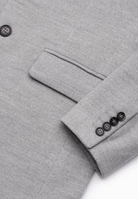 Blazer grigio in lana con superficie texturizzata, taschino sul petto e quattro bottoni neri sul polsino con dettagli di cucitura.