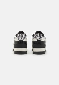 Tênis com padrão de zebra em preto e branco, com um cabedal texturizado, apresentando um calcanhar acolchoado e sola de borracha grossa, projetados para conforto e suporte.