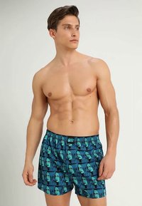 Μπλε μαγιό κοντά με επαναλαμβανόμενο γραφικό σχέδιο προσώπων, ελαστική ζώνη στη μέση και μαλακό υλικό για άνεση.