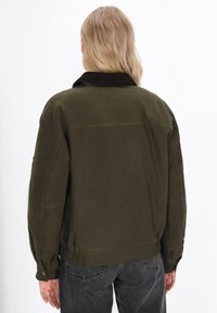 Olivgrüner Bomberjacke mit einem Cordkragen, elastischem Bund und geknöpften Manschetten, die eine glatte, matte Textur und einen oversize Schnitt aufweist.
