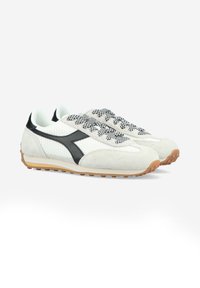 Ljust grå sneakers med en texturerad mocka-övre, svarta detaljer och mönstrade snören. Gummisula med grepp för stabilitet.
