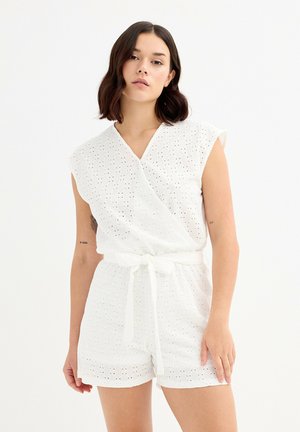 Mono de algodón blanco con diseño envolvente, mangas cortas, patrón de ojetes, cinturón atado en la cintura y pantalones cortos de corte recto. Textura suave.