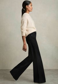 Pull en tricot crème avec une coupe ample et des épaules tombantes, associé à un jean noir à taille haute et jambes larges, doté d'un design à cinq poches.