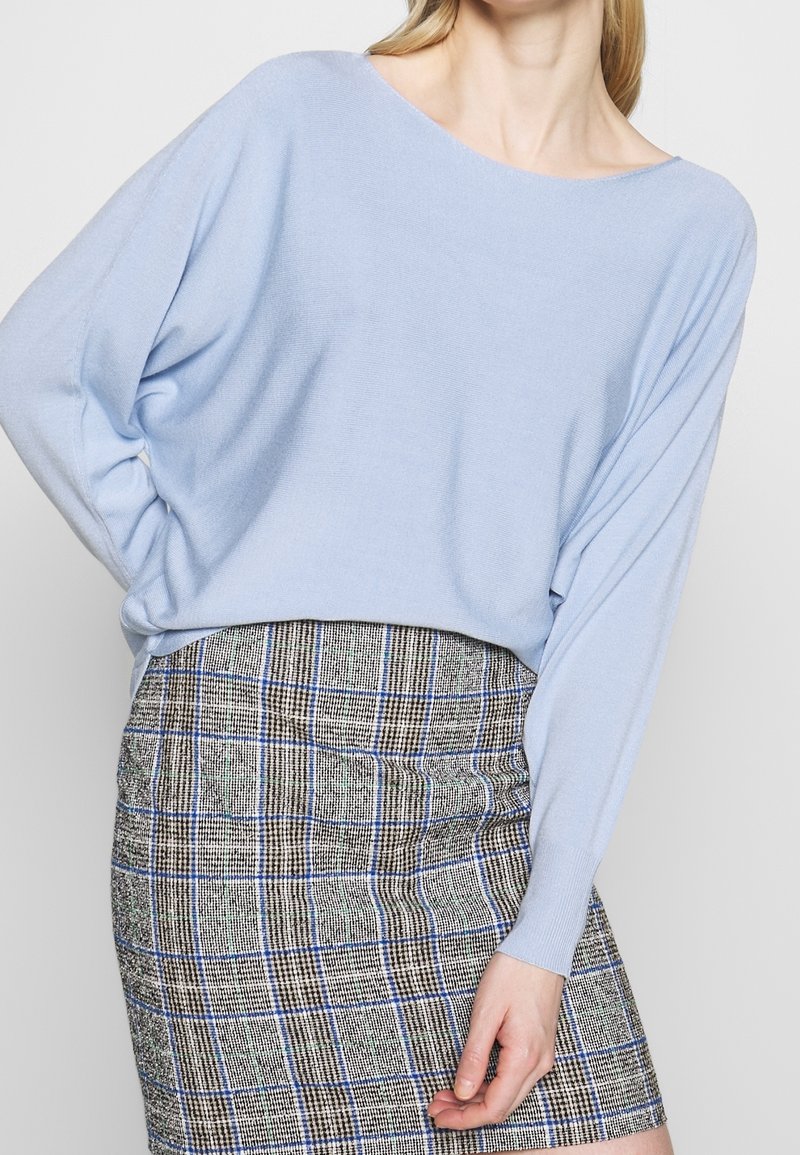 Ljusblå, löst sittande tröja med vid halsringning, kombinerad med en mönstrad rutig kjol i bruna, blå och gröna nyanser.