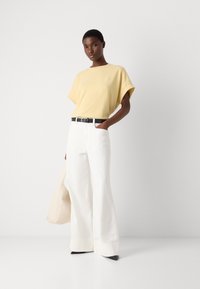 Světle žluté oversized tričko, bílé široké kalhoty, černý pásek a černé lodičky na špičku. Neutrální měkká taška dokončuje vzhled.