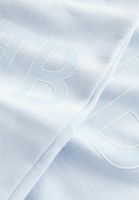Svetlo modrá tkanina s jemnou textúrou a výrazným bielym logom. Materiál vyzerá mäkko a je trochu elastický.