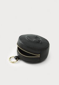 Round black leather pouch with textured surface, gold zipper, and keyring attachment. Features embossed logo on top.