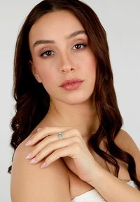 Anello in acquamarina incastonato in argento, con una forma a marquise e dettagli laterali. La modella posa con uno sfondo naturale e armonioso, mettendo in evidenza i dettagli delle mani.