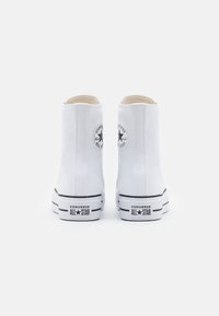 Białe sneakersy za kostkę z płótna, z czarnym logo gwiazdy, czarnymi paskami na podeszwie oraz zaokrąglonym noskiem.