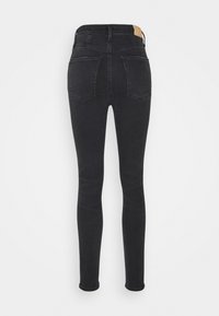 Jeans ajustados negros de cintura alta, fabricados en denim. Incluyen dos bolsillos traseros y un parche de cuero marrón en la cintura.