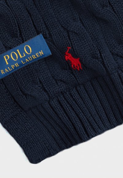 Granatowy sweter robiony na drutach z wzorem w warkocze, ściągacz u dołu i czerwonym haftowanym logo polo; metka mówi "POLO RALPH LAUREN."