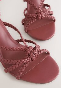 Sandales à talons hauts en cuir tressé rouge avec des détails complexes de noeuds et un design lisse à bout ouvert.