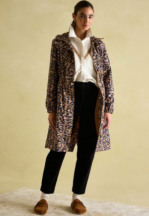 Leopard print waterproof coat with a zip and snap closure, two front pockets, and an adjustable hood. Paired with black pants and brown footwear.