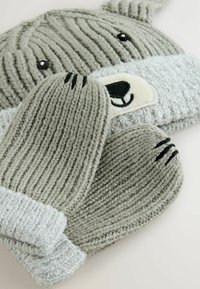 Conjunto de gorro y manoplas de punto gris con un diseño de oso, con costuras texturizadas, acentos negros y un suave puño gris en el gorro.