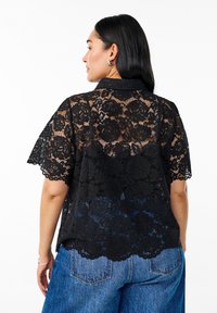Sort blonde skjorte med korte ærmer, der har blomster mønstre, en kravehals og en scallop kant, lagdelt over blå denim jeans.