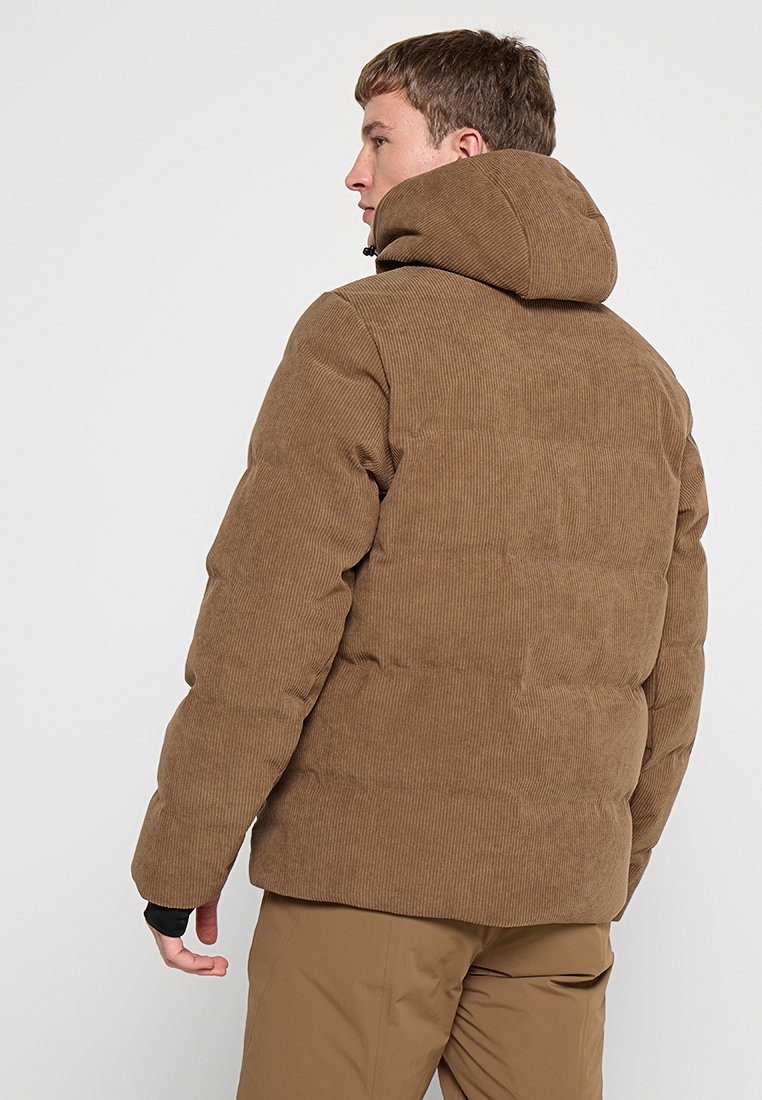 Braune Cord-Puffjacke mit Kapuze, die gesteppten Abschnitte und strukturierten Stoff zeigt. Das Modell ist gedreht und präsentiert das Rückendesign.