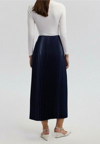 Lunga gonna plissettata blu navy realizzata in tessuto leggero, abbinata a un top aderente a maniche lunghe bianco. Indossata con scarpe con zeppa bianche.