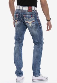 Blaue Jeans aus Denim mit geradem Bein, ausgestattet mit detaillierten Nähten und bestickten Gesäßtaschen. Abgerundet mit einem kontrastierenden Gürtel und weißen Sneakern.