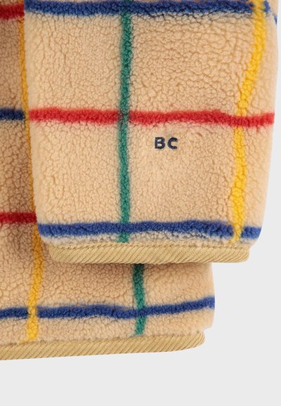 Coperta in pile di colore crema con motivo a quadri in rosso, blu, verde e giallo. Presenta un bordo piegato e una piccola etichetta stampata "BC". Tessuto morbido.