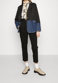 Svart och denimjacka med långa ärmar och krage, i kombination med svarta byxor och beige snörskor. Noterbar sjal detalj vid halsen.