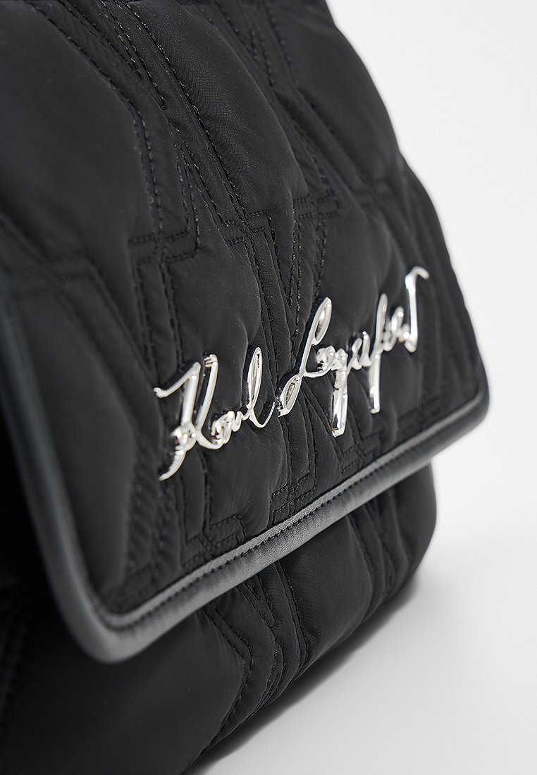 Sac à main noir matelassé avec un détail logo argenté à l'avant, d'une texture lisse et avec un design à rabat.