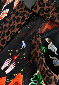 Többszínű szövet, amely leopárdmintát, részletes virágmotívumokat, valamint szemeket és kezeket ábrázoló szimbólumokat tartalmaz. Simább textúra élénk színekkel.