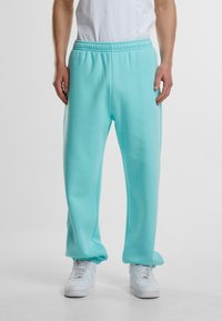 Turkise joggebukser laget av myk stoff med elastisk midjebånd, med en avslappet passform og ribbede anklene, kombinert med hvite sneakers.