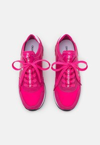 Zapatillas deportivas rosas con parte superior de tela texturizada, acentos blancos y suela negra contrastante. Los cordones son gruesos y están ajustados de manera prominente.